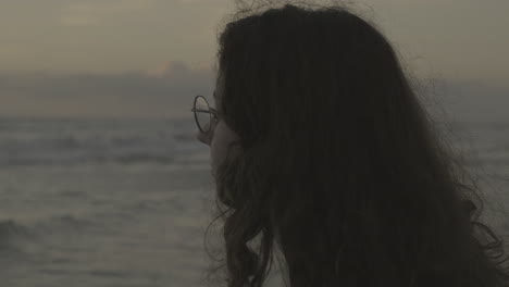 Young-female-wearing-glasses-looking-out-across-stormy-overcast-ocean-waves,-head-shot