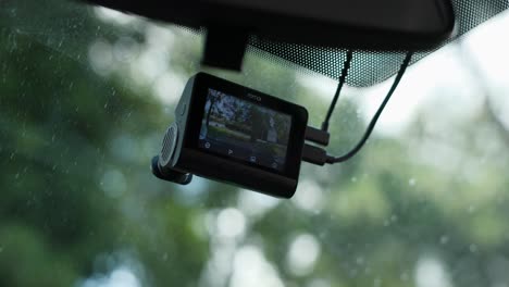 Close-up-view-of-a-dashcam-mounted-on-a-car-windscreen-with-an-outdoor-scene-in-the-background,-captured-during-daylight