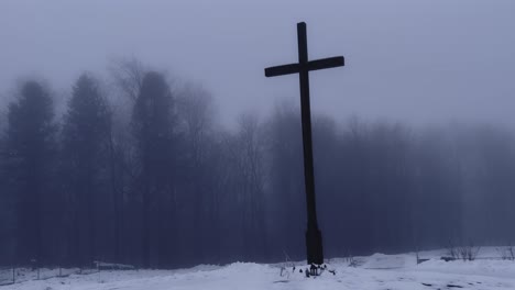 De-Izquierda-A-Derecha,-Un-Vídeo-Panorámico-En-4K-De-Una-Gran-Cruz-Oscura-Frente-A-Un-Bosque-Brumoso-En-Invierno.