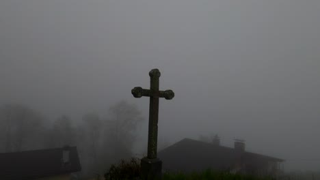 4K-video-panning-across-a-small-stone-cross-in-a-foggy,-misty-landscape-in-Switzerland,-Alps