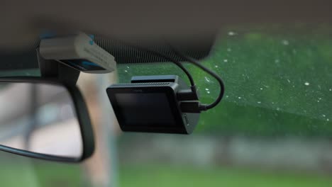 Close-up-of-a-dashcam-mounted-on-the-windscreen-of-a-car,-capturing-the-outside-view-including-a-walking-person-in-the-background