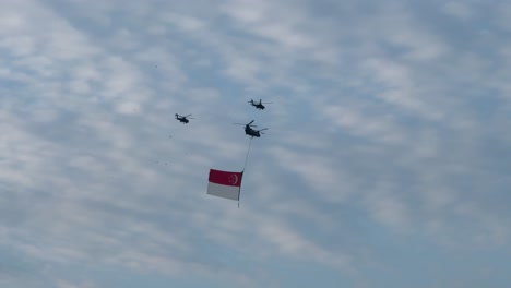 Un-Helicóptero-De-Carga-Pesada-Lleva-La-Bandera-Del-Estado-Escoltado-Por-Dos-Helicópteros-De-Ataque-Apache-Durante-El-Desfile-De-Ensayos-Del-Día-Nacional-De-Singapur