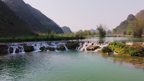 Dieses-Drohnenvideo-Zeigt-Eine-Ruhige-Szene-Im-Phong-Nam-Tal-In-Cao-Bang,-Nordvietnam.-Es-Zeigt-Einen-Sanften-Wasserfall,-Der-In-Einen-Ruhigen-Blauen-Fluss-Mündet.