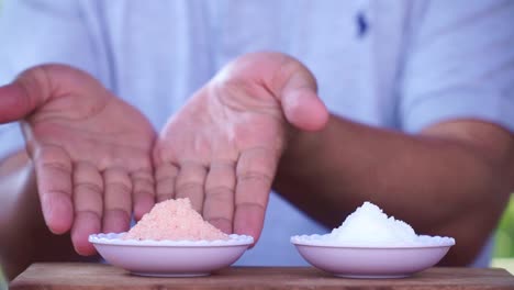 Two-palm-of-people-showing-Pink-himalayan-salt-and-white-crystal-salt-on-the-white-small-bowl