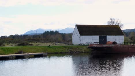 Malerische-Schottische-Aussicht-Auf-Das-Alte-Rustikale-Bootshaus-Aus-Stein-Und-Das-Boot-Am-Caledonian-Canal-In-Fort-Augustus-Im-Hochland-Von-Schottland,-Großbritannien