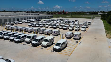 Slowly-dropping-drone-shot-of-USPS-delivery-trucks-behind-large-post-office-viewed-from-the-corner-of-the-parking-lot