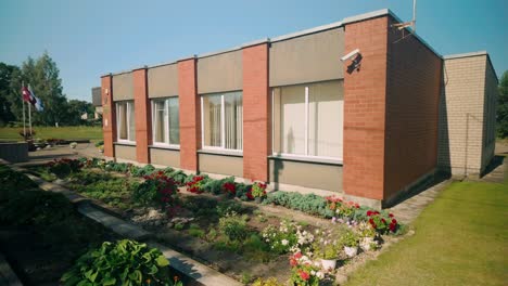 Fachada-Del-Edificio-De-Administración-De-La-Parroquia-De-Kaplava-En-Letonia,-Que-Muestra-Su-Exterior-Con-Un-Jardín-Lleno-De-Flores.