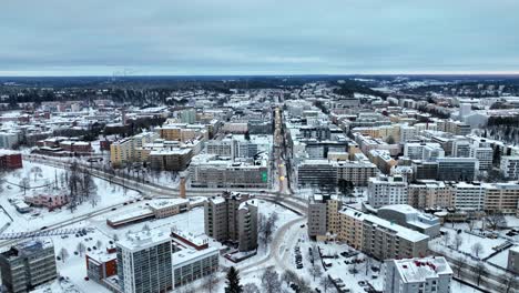 Drone-flying-backwards-over-streets-in-Lahti-city,-dark,-winter-day-in-Finland