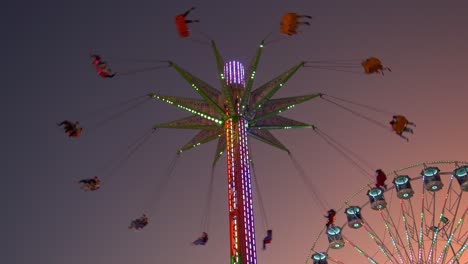 Illuminated-sky-flyer-festival-ride,-swinging-up-high-in-the-sky-against-sunset-dusk-sky