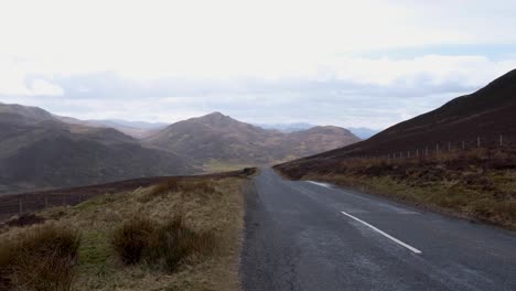 Remote-empty-road-in-mountainous-landscape-of-highlands-of-Scotland-with-tussock-grass-and-golden-brown-terrain-in-outdoor-wilderness