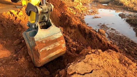 Excavator-digging-a-trench-in-red-iron-rich-earth-on-sandy-bank-to-manage-water-flow-responsibly---in-slow-motion