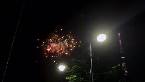 Los-Fuegos-Artificiales-Iluminan-El-Cielo-Nocturno-Con-Ráfagas-De-Color-Rojo-Cerca-De-Una-Alta-Torre-Iluminada.