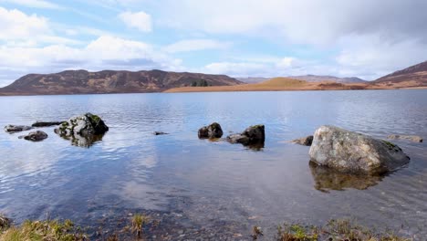 Scenic-landscape-view-overlooking-Scottish-loch-of-freshwater-with-rocky-boulders-and-mountainous-terrain-in-highlands-of-Scotland-UK