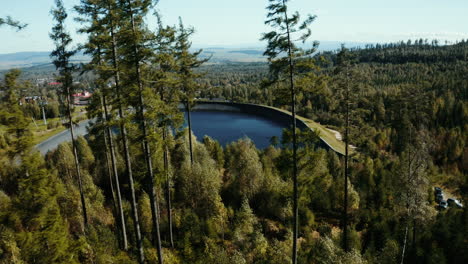 Toma-Aérea-De-Un-Dron-Que-Se-Mueve-Desde-Los-árboles-Sobre-La-Presa-De-Agua-Hasta-Un-Pueblo-En-Los-Altos-Tatras,-Mostrando-árboles-Verdes-De-Verano,-Colinas-Y-Montañas-En-Eslovaquia,-Europa