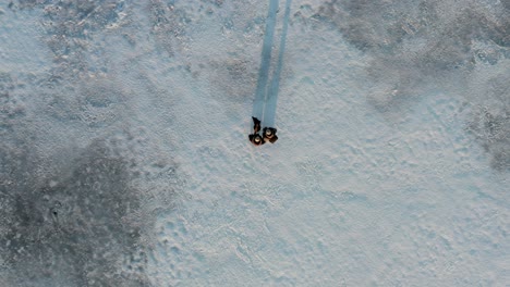 Top-Down-Drone-Shot-of-Couple-with-Labrador-on-Frozen-Lake-at-Sunset