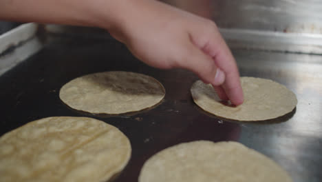 Amazing-slow-motion-shot-of-a-professional-chef's-hand-using-his-fingers-to-lift-and-flip-Mexican-tortillas-placed-on-a-large-industrial-cooking-griddle-in-a-Mexican-restaurant