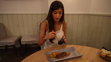 Woman-adding-sauce-to-food-in-cozy-restaurant-setting,-evening