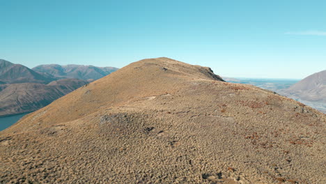 Peak-Hill-Covered-In-Brown-Tussock-With-Lake-Coleridge-In-Background-New-Zealand-Drone-Descend