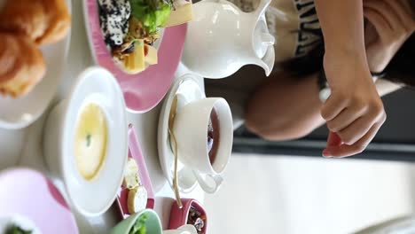 A-woman-puts-a-cube-of-sugar-in-her-tea-beside-a-delicious-breakfast-in-fancy-restaurant-close-up-shot,-vertical-video,-insert-shot