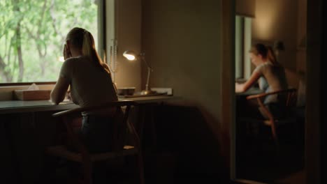 A-woman-sitting-at-a-desk-writing-on-a-notebook-in-front-of-a-wide-window-with-natural-scenes-outside