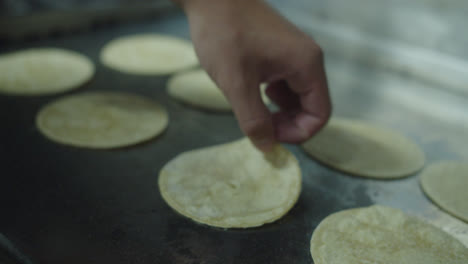 Beautiful-general-slow-motion-shot-of-a-chef-flipping-a-group-of-Mexican-tortillas-placed-on-a-large-griddle-in-an-industrial-kitchen-by-hand