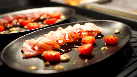 Chef-adds-half-a-tomato-to-grilled-fish-on-sizzling-plates-in-a-restaurant-kitchen,-close-up