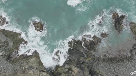 Top-down-shot-of-sea-waves-splashing-on-hitting-the-volcanic-rocks-at-coastline