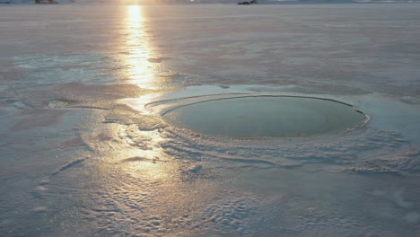 Toma-Aérea-De-Un-Agujero-En-El-Hielo-Con-Reflejo-Del-Atardecer-Tomada-Desde-Un-Dron-Inclinado-Hacia-Abajo