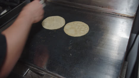 Amazing-general-slow-motion-shot-of-a-professional-Mexican-chef-placing-tortillas-on-a-large-griddle-in-an-industrial-kitchen-inside-a-restaurant