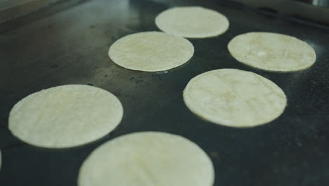 Beautiful-medium-shot-of-a-set-of-Mexican-tortillas-cooking-on-an-industrial-griddle-in-a-Mexican-restaurant-kitchen-in-Spain