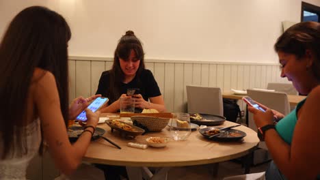 Spanish-girls-in-a-restaurant-finishing-their-meal,-laughing-and-scrolling-on-phones