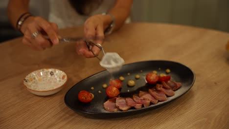 Garnishing-a-gourmet-dish-with-sauce-on-a-black-plate,-shot-in-a-restaurant-table