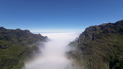 Gorgeous-rainbow-over-clouds-covering-valley-between-lush-rugged-green-peaks-of-mountains-on-Madeira-Island,-Portugal