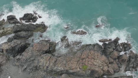 Top-shot-of-waves-hitting-the-rocks-on-coastline-of-a-turquoise-sea