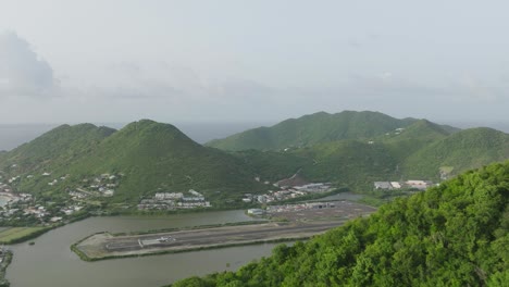 Toma-Aérea-En-Movimiento-Del-Aeropuerto-Grand-Case-Con-Avión-Saliendo-De-Saint-Martin-Con-Un-Hermoso-Paisaje-Caribeño-De-Fondo