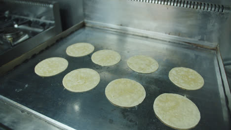 Beautiful-slow-motion-shot-of-a-group-of-Mexican-tortillas-cooking-on-a-griddle-in-an-industrial-kitchen-in-a-Mexican-restaurant