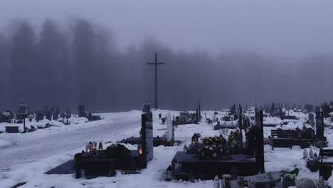 4k-Aufnahme-Eines-Polnischen-Friedhofs-Im-Winter-Mit-Grabsteinen-Und-Einem-Großen-Kreuz-Vor-Einem-Nebligen-Wald