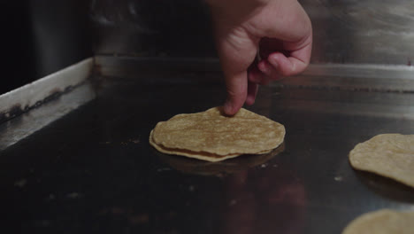 Amazing-Close-up-slow-motion-shot-of-a-professional-chef's-hand-using-his-fingers-to-lift-and-flip-Mexican-tortillas-placed-on-a-large-industrial-cooking-griddle-in-a-Mexican-restaurant