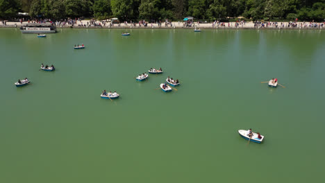 Beautiful-general-drone-shot-of-the-large-pond-in-El-Retiro-park-with-boats-sailing-during-a-summer-morning