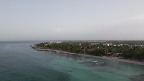 Drone-view-panorama-of-Bayahibe-beach-during-sunny-day,-where-people-enjoys-vacation-on-clear-Caribbean-sea-shore-in-Dominican-Republic