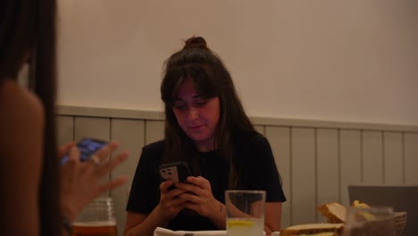 Close-up-of-woman-with-friend-at-restaurant-table-using-smartphone