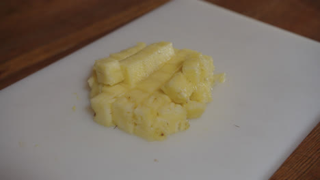 Beautiful-slow-motion-close-up-shot-of-a-set-of-small-pineapple-pieces-placed-on-a-white-chopping-board-on-a-bar-counter-with-dim-white-lighting