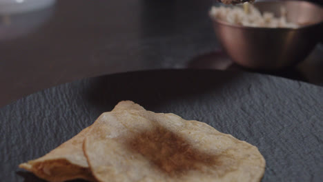 Hermosa-Toma-En-Cámara-Lenta-De-Un-Chef-Que-Sirve-Pollo-Desmenuzado-De-Un-Tazón-En-Tortillas-Mexicanas-Colocadas-En-Un-Plato-De-Presentación-Negro