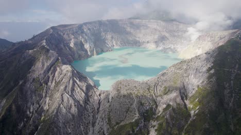 Aerial-Circling-The-Rim-Of-A-Steaming-Volcano-Ijen-with-a-Turquoise-Lake,-and-foggy-cloudy-Mountain-in-the-background---East-Java,-Indonesia