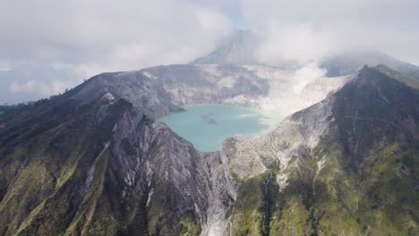 Aerial-Circling-The-Rim-Of-A-Steaming-Volcano-Ijen-with-a-Turquoise-Lake,-and-foggy-cloudy-Mountain-in-the-background---East-Java,-Indonesia