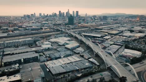 A-drone-shot-of-the-Ribbon-Of-Light-6th-Street-Bridge-during-sunset-in-Los-Angeles-California-with-cars-driving-in-the-foreground-of-the-city's-skyline-from-about-300-feet-above-the-ground