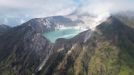 Aerial-Circling-The-Rim-Of-A-Steaming-Volcano-Ijen-with-a-Turquoise-Lake,-and-foggy-cloudy-Mountain-in-the-background---East-Java,-Indonesia