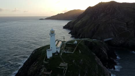 South-Stack-lighthouse-aerial-rising-view-of-rugged-island-mountain-range-during-golden-hour-sunrise