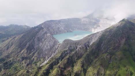 Aerial-Circling-The-Rim-Of-A-Steaming-Volcano-Ijen-with-a-Turquoise-Lake,-and-foggy-cloudy-Mountain-in-the-background---East-Java,-Indonesia