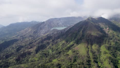 Vista-Aérea-Que-Rodea-El-Borde-De-Un-Volcán-Humeante-Ijen-Con-Un-Lago-Turquesa-Y-Una-Montaña-Nublada-Y-Brumosa-Al-Fondo---Java-Oriental,-Indonesia